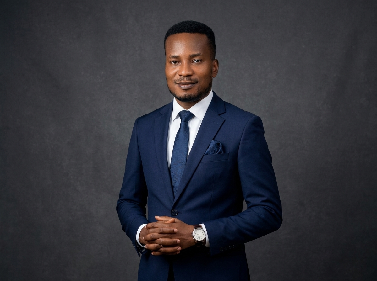 Amb. John Ifeanyi Amos standing in dark corporate business suit with confident leadership posture